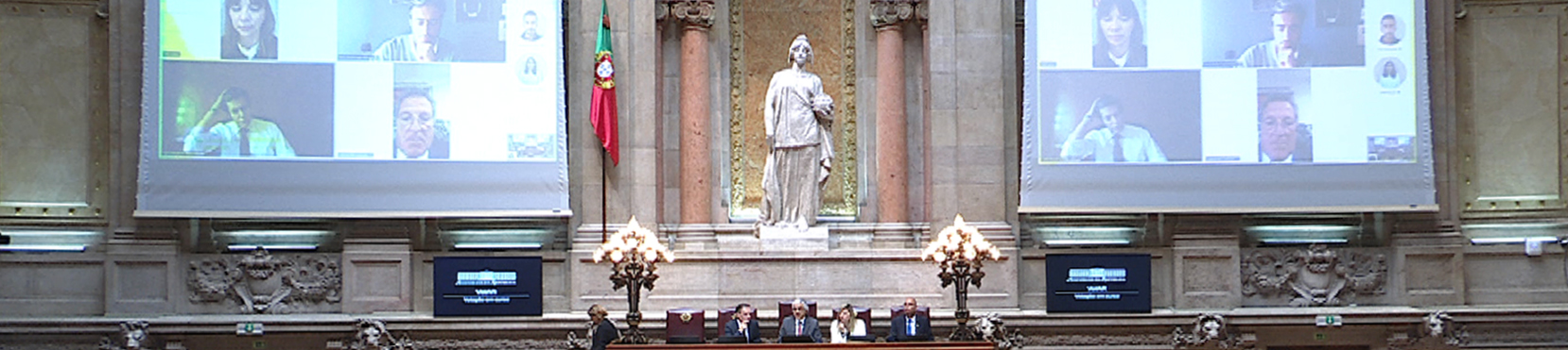 Imagem da Sala das Sessões com duas telas com imagem dos Deputados que assistem remotamente